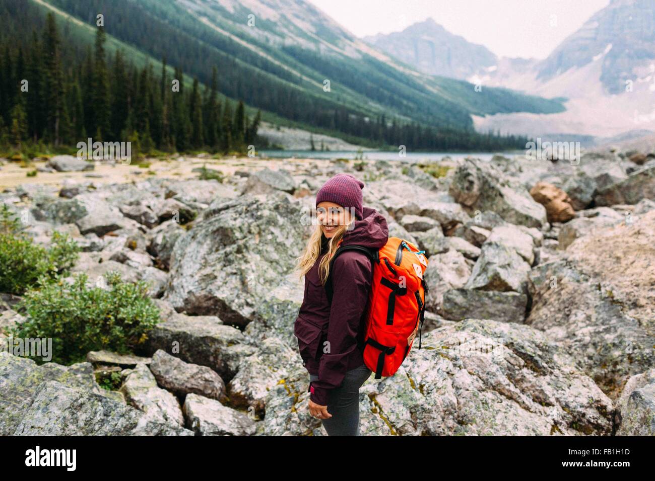 Seitenansicht Mitte Erwachsene Frau steinigen Landschaft tragen Rucksack Kamera lächelnd Moraine Lake Banff Nationalpark Alberta Kanada Stockfoto