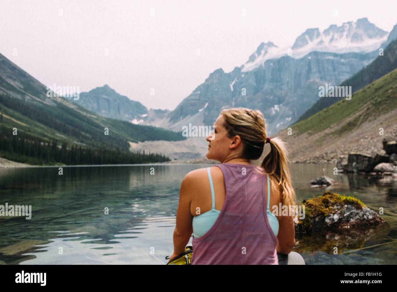Ansicht von hinten Mitte erwachsenen Frau sitzen am Rand des Wassers wegsehen, Moraine Lake, Banff Nationalpark, Alberta Kanada Stockfoto