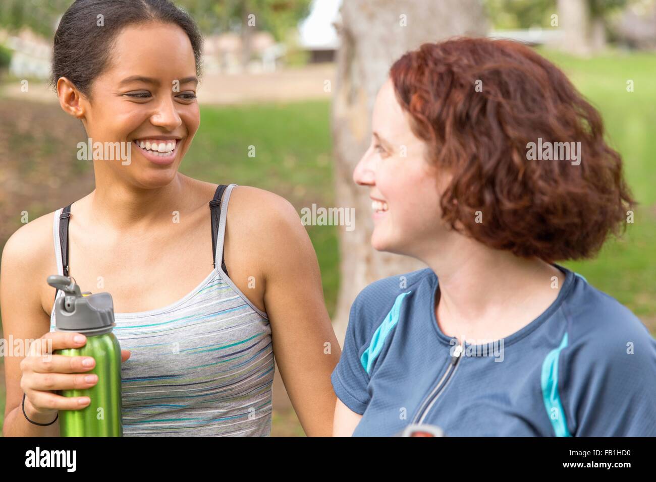 Kopf und Schultern der jungen Frauen, die Wasserflaschen von Angesicht zu Angesicht lächelnd Stockfoto