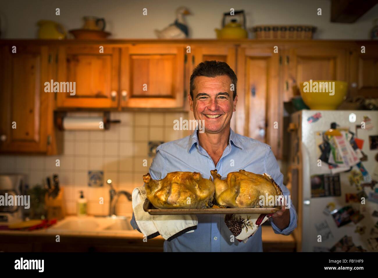 Porträt von reifer Mann hält Grillhähnchen in Küche Stockfoto