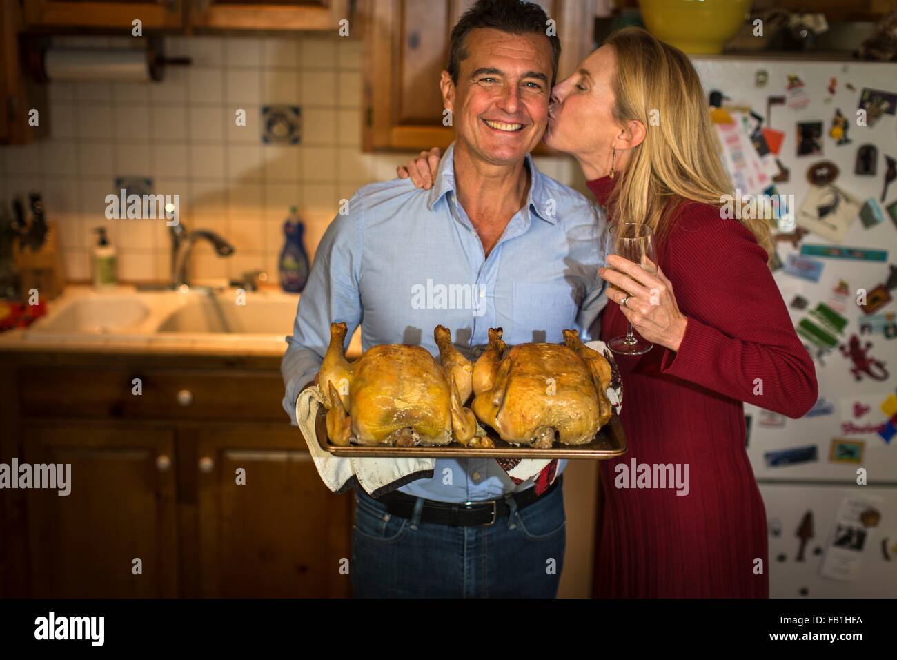 Porträt des reifes Paar halten Grillhähnchen in Küche Stockfoto