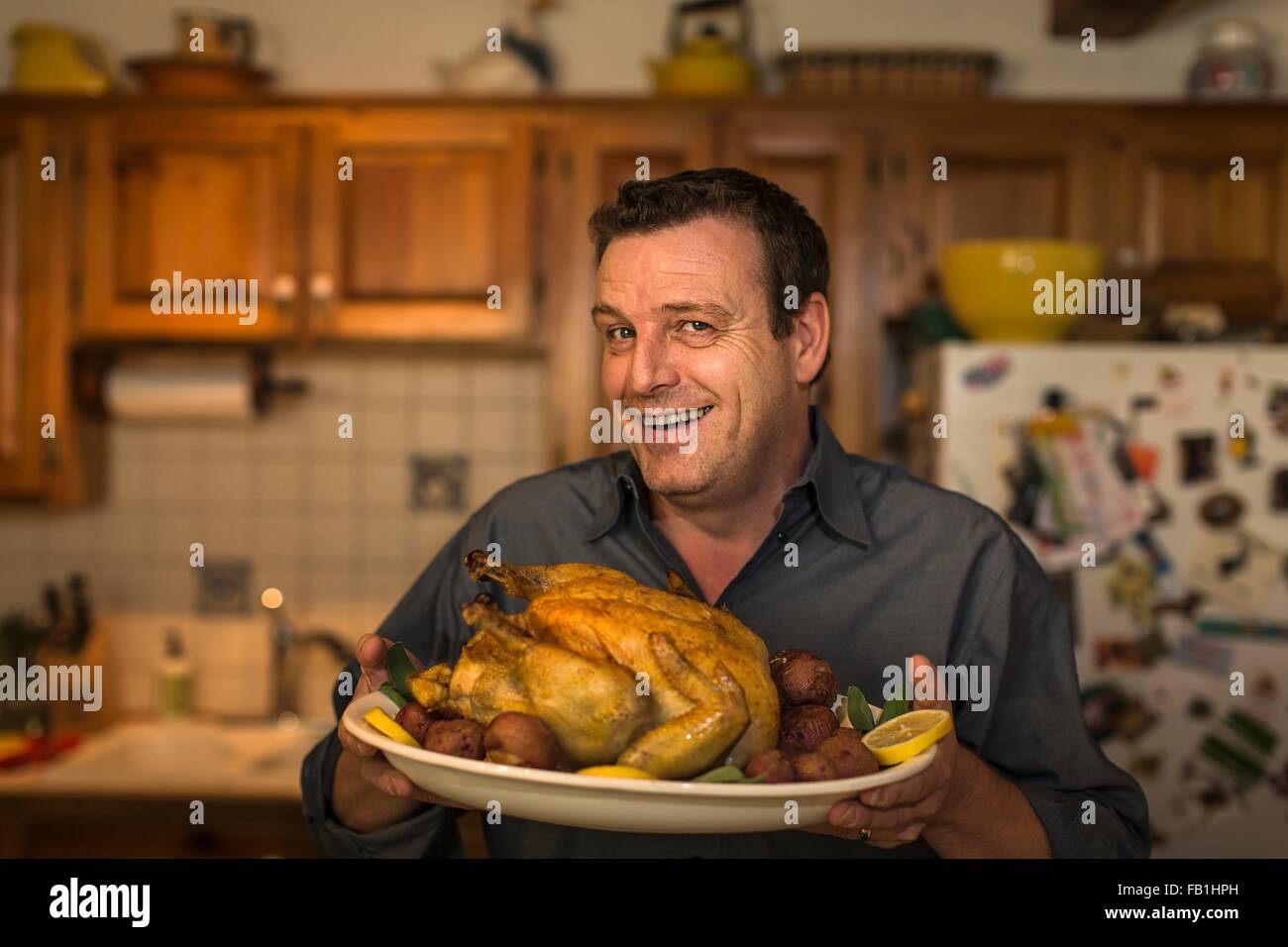 Porträt von reifer Mann halten Braten Huhn Abendessen in Küche Stockfoto