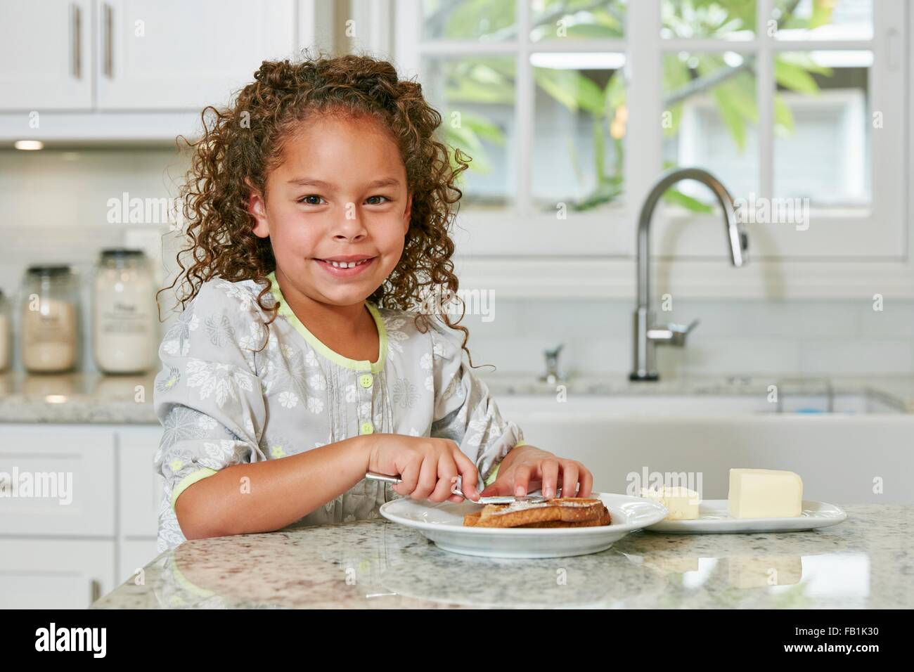 Mädchen an der Küche Zähler Verbreitung Butter auf Toast, Blick auf die Kamera zu Lächeln Stockfoto