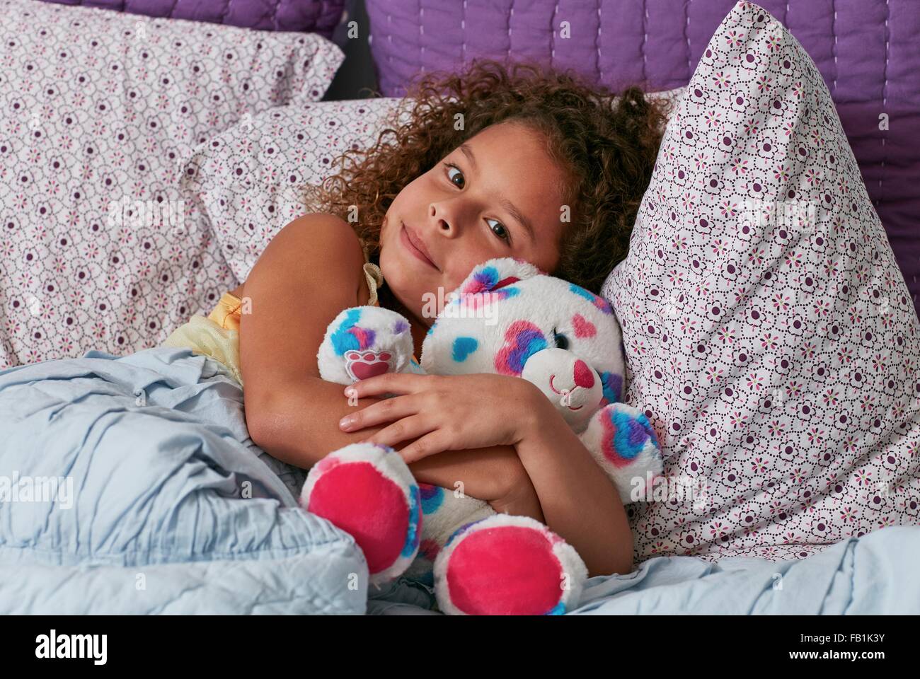 Mädchen im Bett kuscheln Teddybär Blick in die Kamera Stockfoto