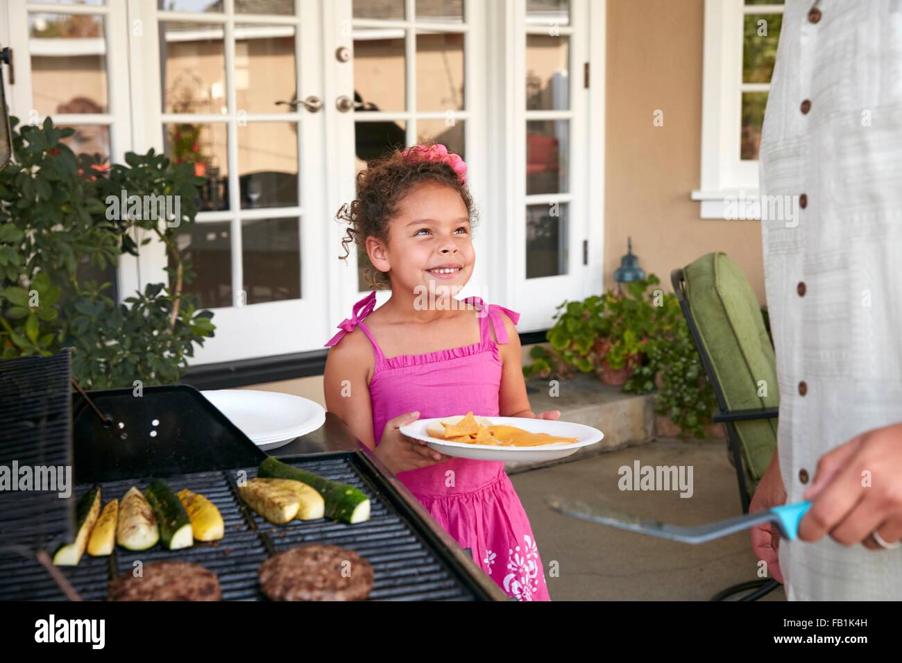 Mädchen auf der Terrasse halten Platte wird Speisen Grill von Vater Stockfoto