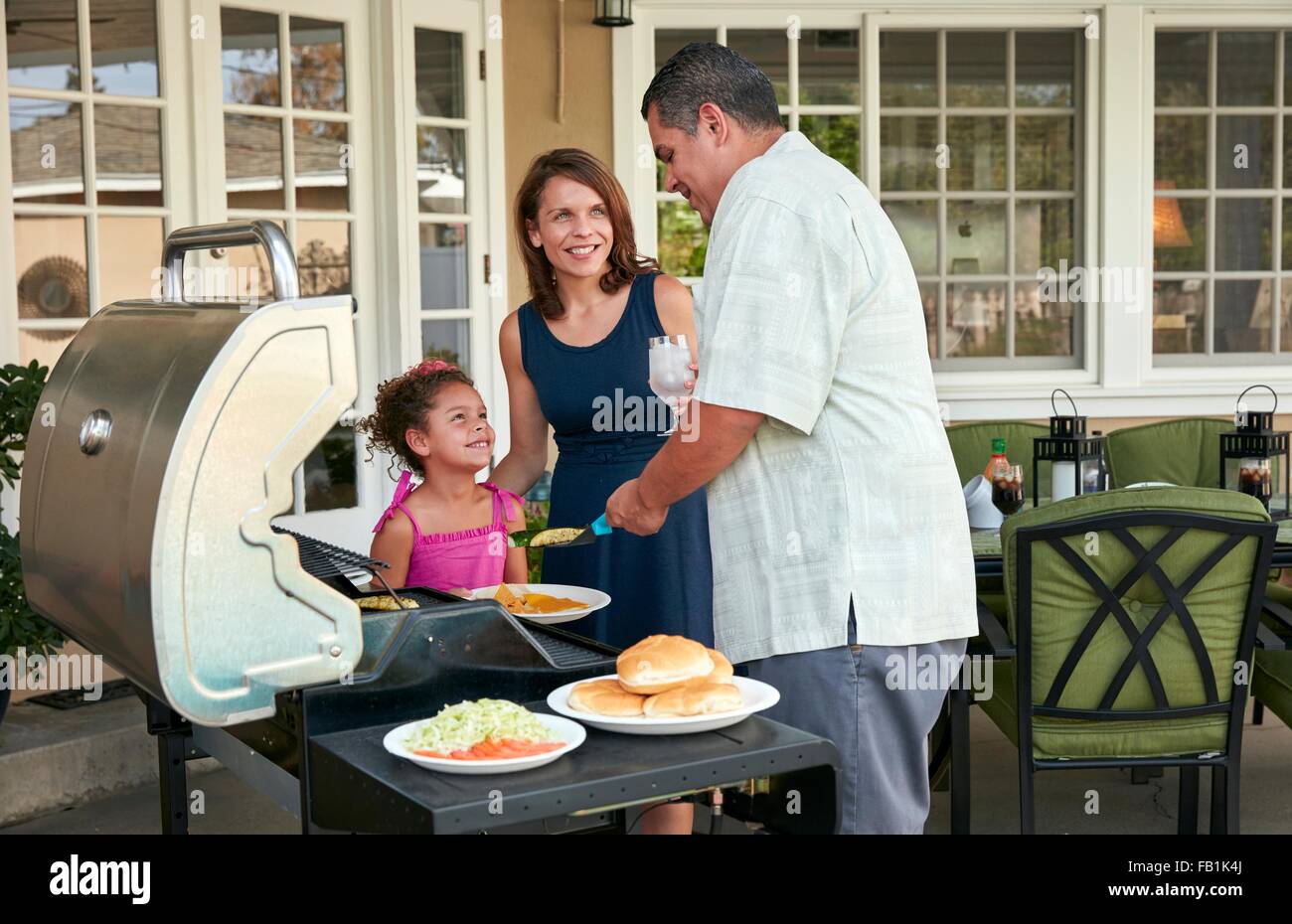 Mutter und Mädchen auf Terrasse Halteplatte Grill Essen serviert wird, von Vater Stockfoto
