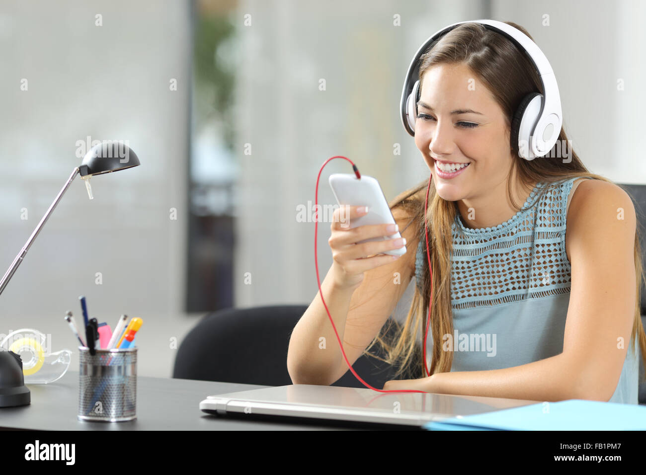 Mädchen, die Ihre Musik mit einem Smartphone und Kopfhörer auf ihrem Desktop zu Hause Stockfoto