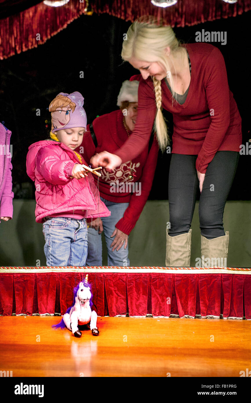 ein 3-jähriges Mädchen lernt, wie man eine Einhorn Marionette an ein Theater im Freien bei einem Christmas Festival in Lake Forest, Kalifornien tätig. Stockfoto