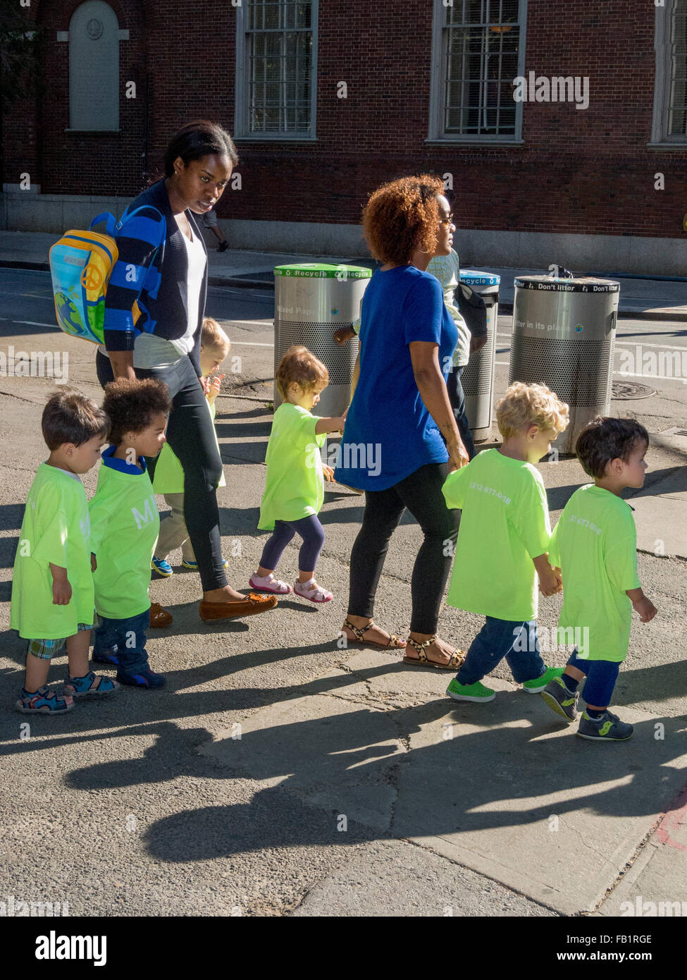 Kita Kleinkinder in passenden grünen t-Shirts werden begleitet von afroamerikanischen Betreuungspersonen in Greenwich Village, New York City. Stockfoto