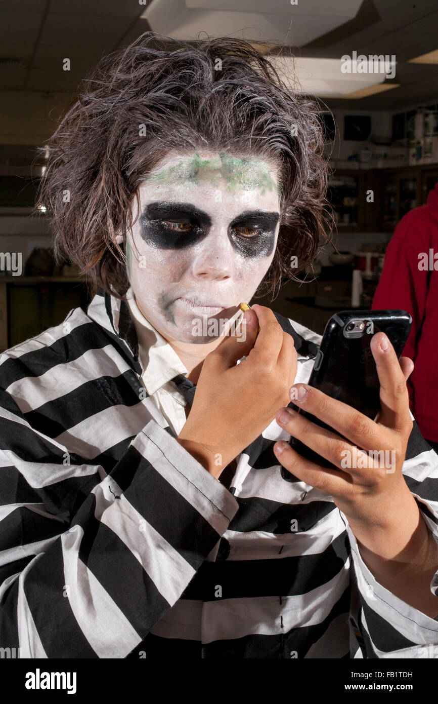 Mit einer Handy-Kamera wie ein Spiegel, ein San Clemente, CA, setzt High-School-Mädchen auf groteske Make-up für Halloween. Beachten Sie gestreifte Kostüm. Stockfoto