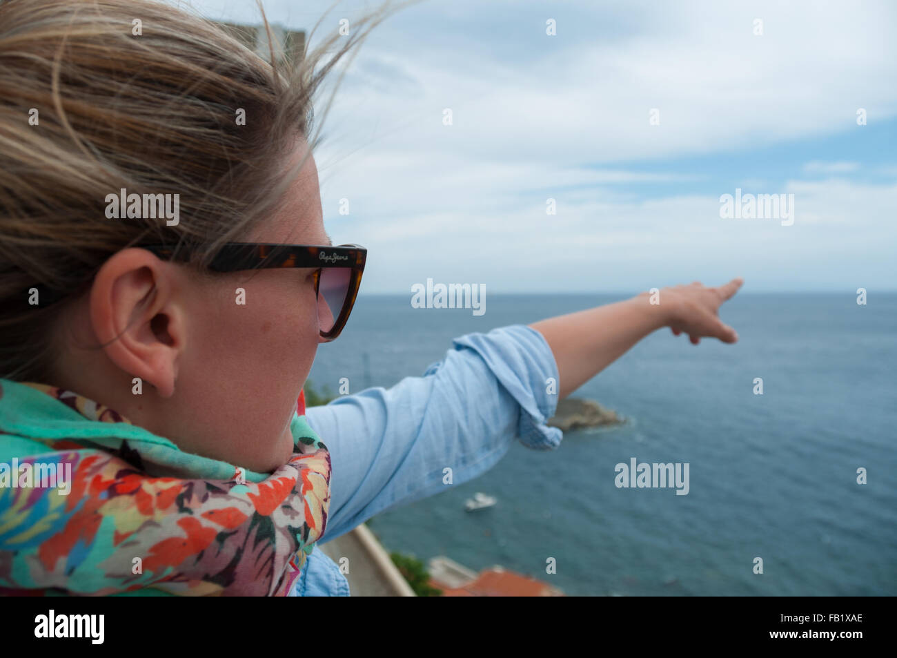 Junge, blonde Frau zeigt mit Finger in Richtung Ozean Horizont Stockfoto