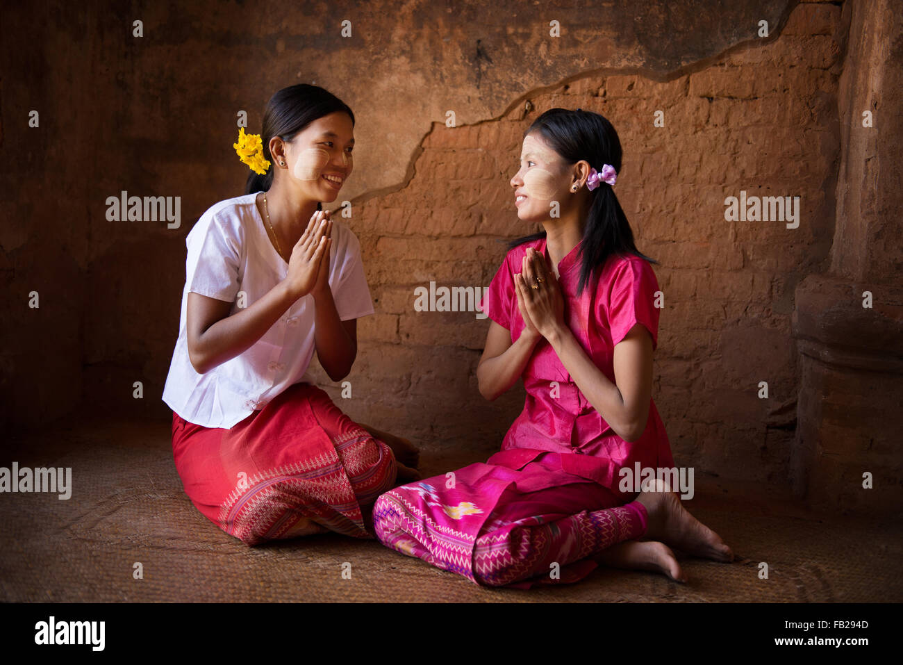 Zwei junge Myanmar Mädchen in eine traditionelle einladende Geste, sitzen im inneren Tempels. Stockfoto