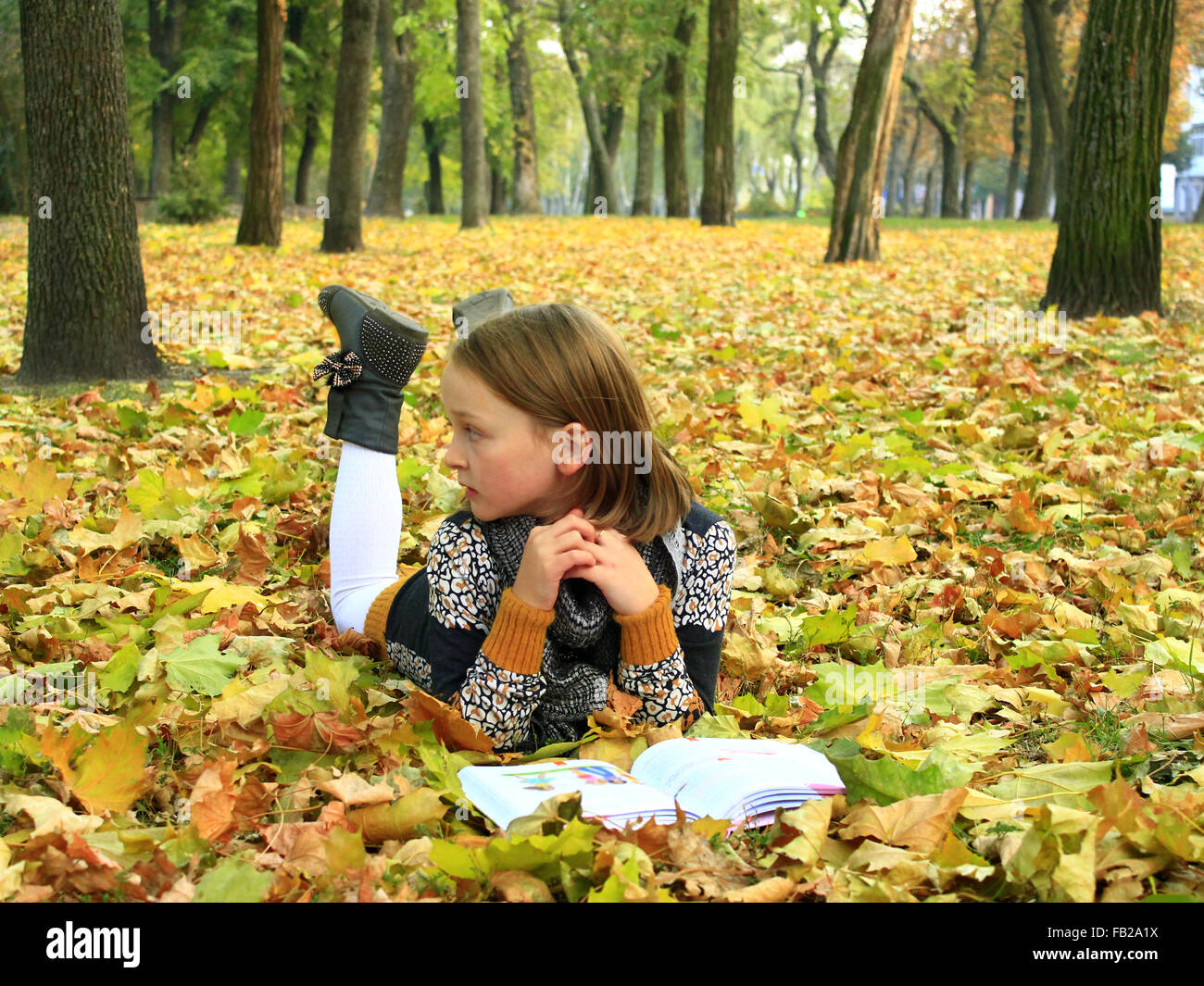 junges Mädchen liest ein Buch im Herbst Park auf dem Boden liegend Stockfoto