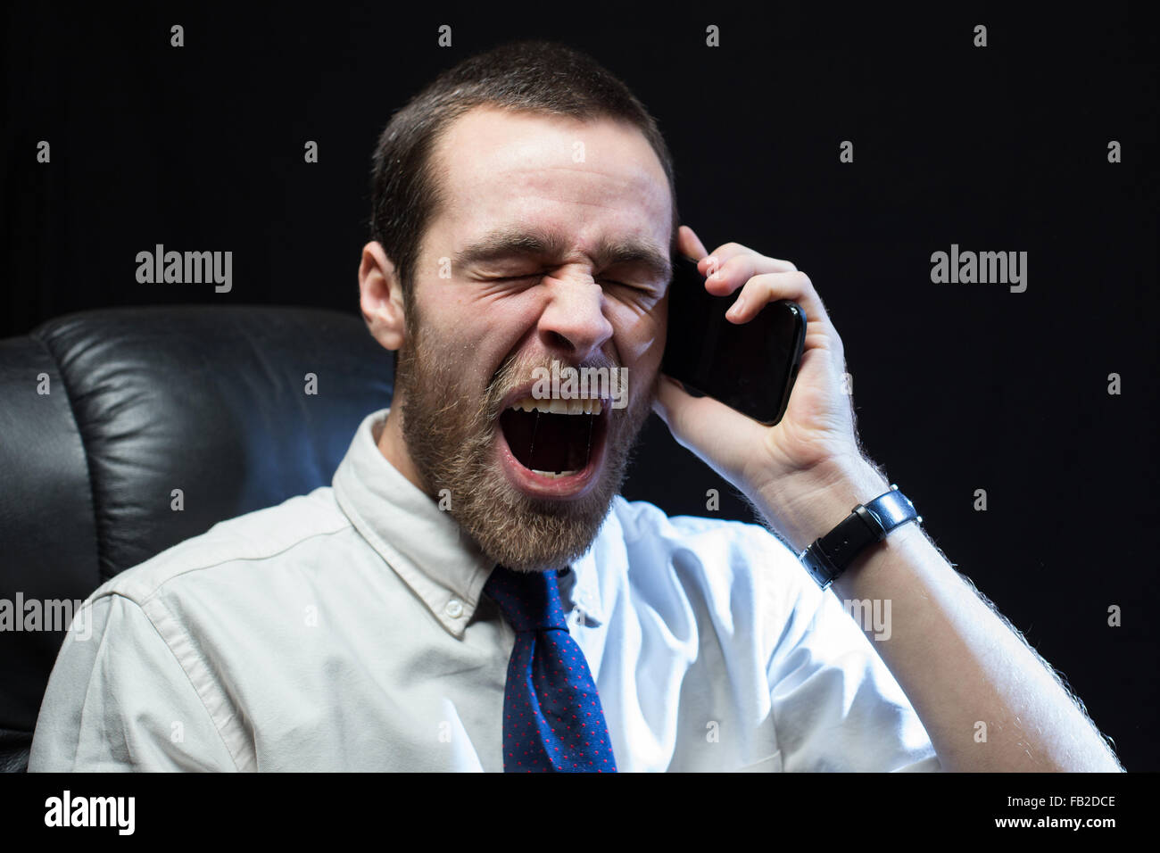 Ein Büroangestellter, trug ein Hemd und Krawatte, schreit nach unten ein Mobiltelefon im Zorn. Stockfoto