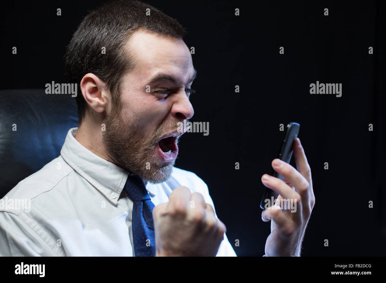 Ein Büroangestellter, trug ein Hemd und Krawatte, schreit nach unten ein Mobiltelefon im Zorn. Stockfoto