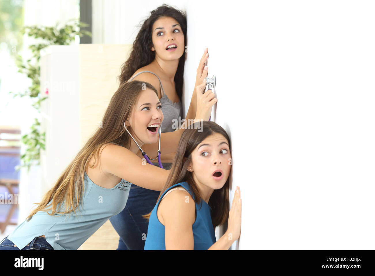 Drei Klatsch-Mädchen durch die Nachbarn Wand zu Hause hören Stockfoto