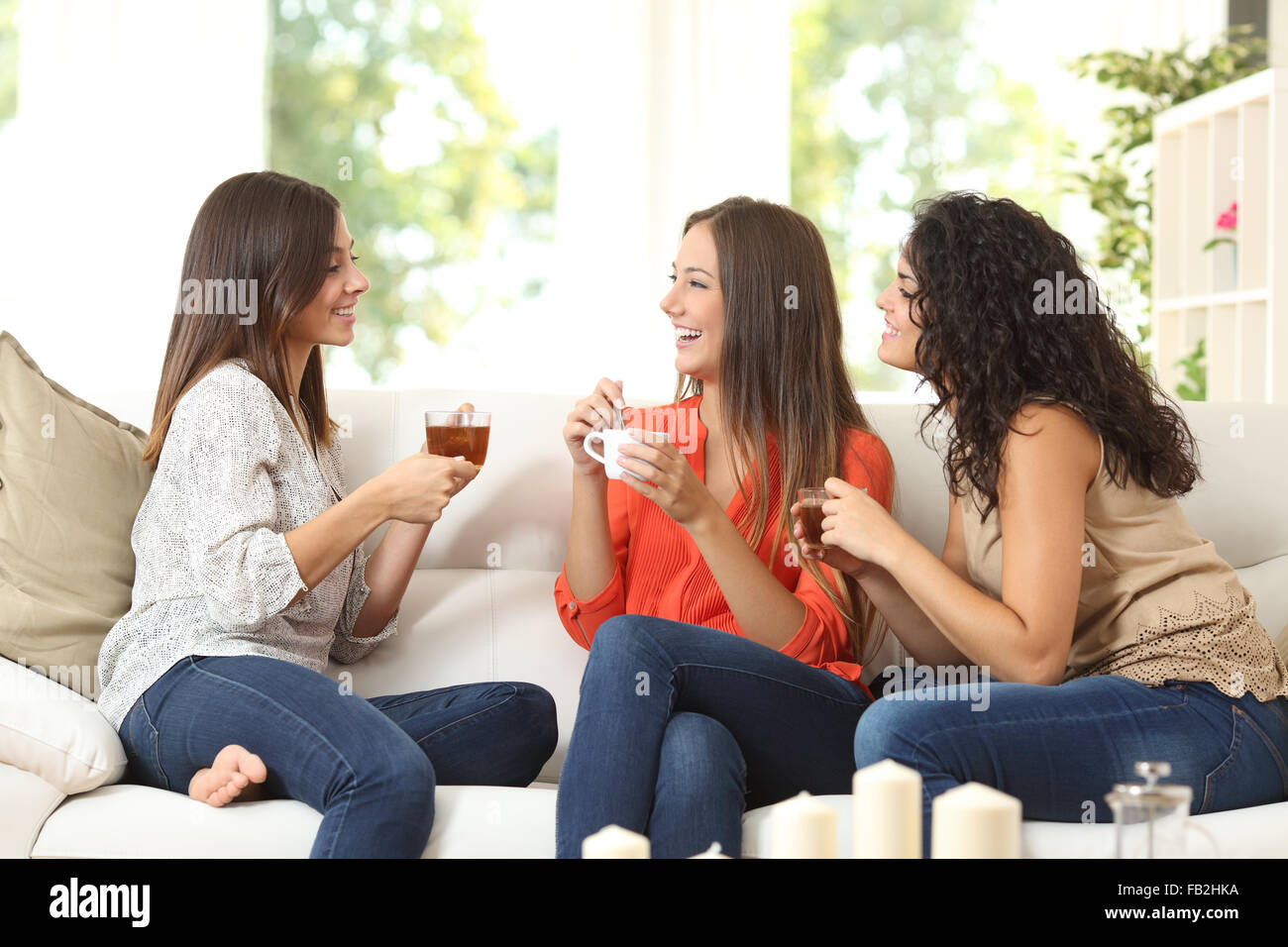 Drei glückliche Freunde reden und trinken Kaffee und Tee auf der Couch zu Hause sitzen Stockfoto