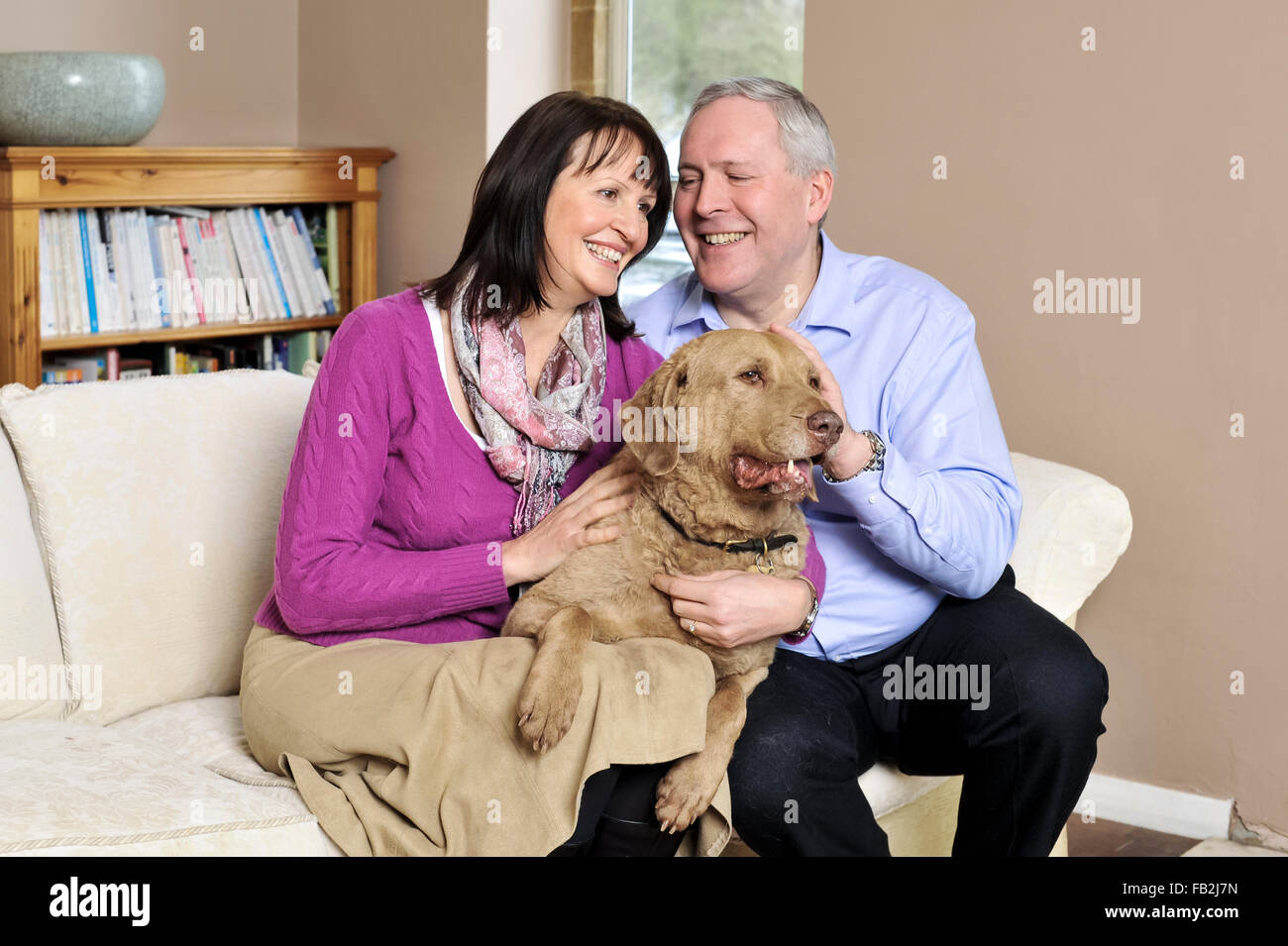 Ein paar mittleren Alters saß auf dem Sofa umarmt ihren Hund Stockfoto