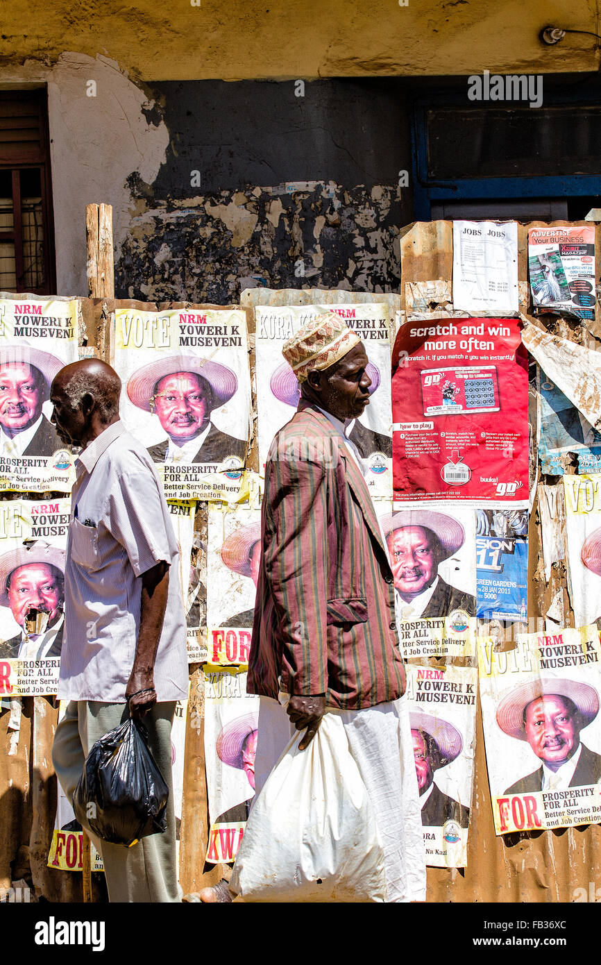 Bürgerinnen und Bürger vorbei an einer Wand voller Wahlpropaganda Förderung des ugandischen Präsidenten Mueveni und seiner Partei NRM für die Gattungen Stockfoto