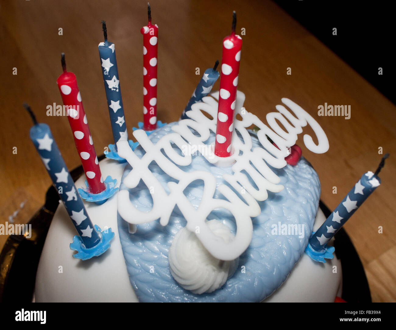 Blau und Weiß Kuchen mit einem Happy Birthday Schild oben und sechs blaue und rote Kerzen auf es auf einem Holztisch. Stockfoto