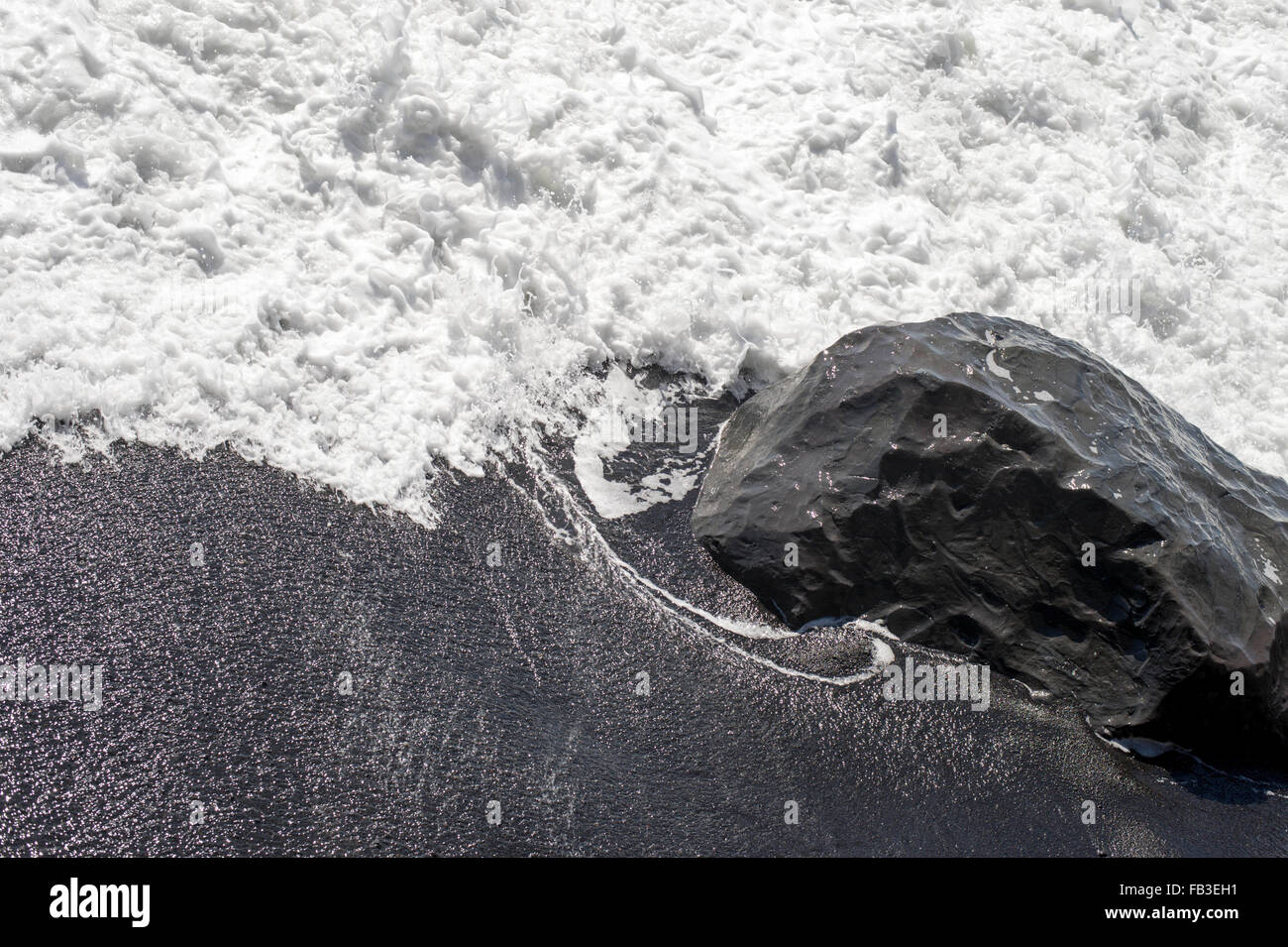 Meerwasser stürzt über einen Basaltfelsen am schwarzen Sandstrand in der Nähe von Vik, Island Stockfoto