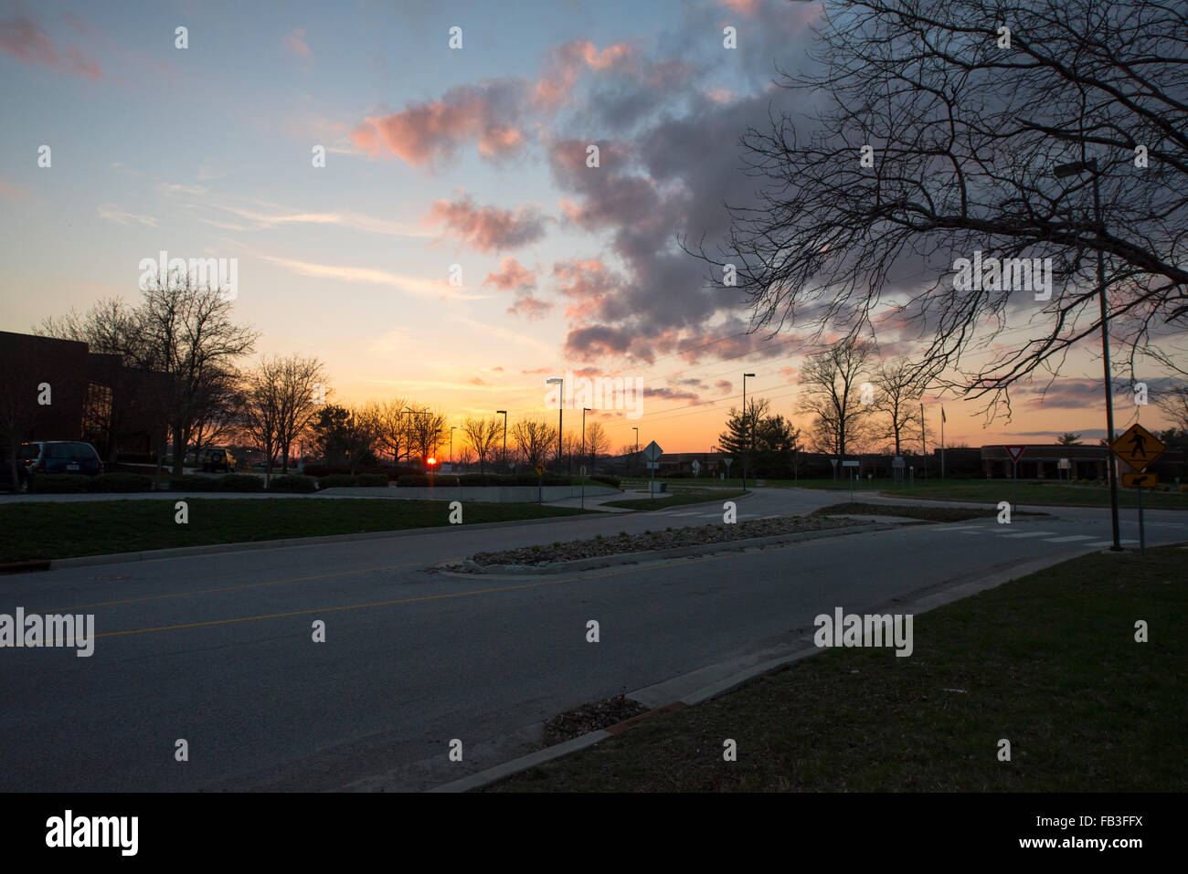 Bewölkt, tief orange und Lachs Sonnenuntergang über einer Straße mit Baum im Vordergrund Stockfoto