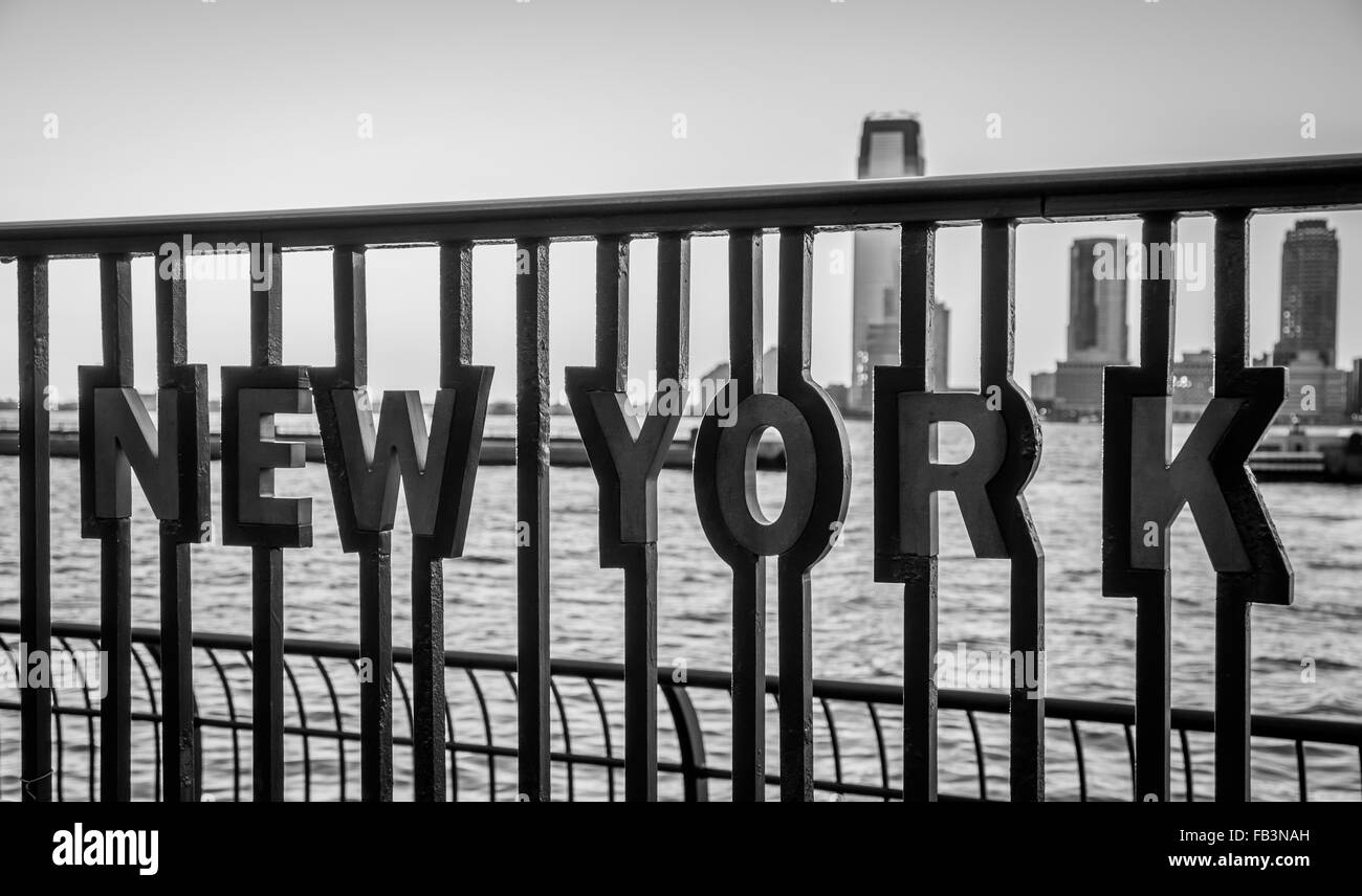 "New York" Einschub in Metallgeländer an das World Financial Center Plaza mit der Hudson River und Jersey City Skyline hautnah Stockfoto