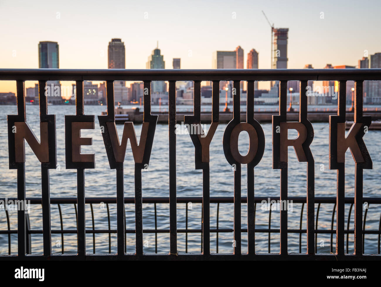 "New York" Einschub in Metallgeländer an das World Financial Center Plaza bei Sonnenuntergang mit dem Hudson River und Jersey City skyline Stockfoto