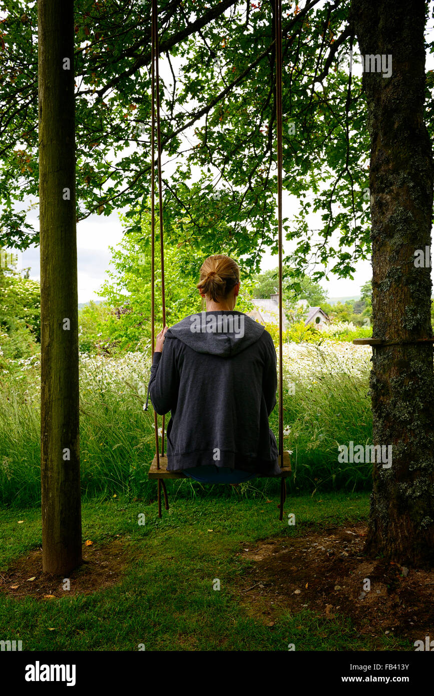 Frau sitzen, sitzen auf der Schaukel hängen hängenden Baum Gartenpark Parkland Blume Blumen Blüte Sommer Stockfoto