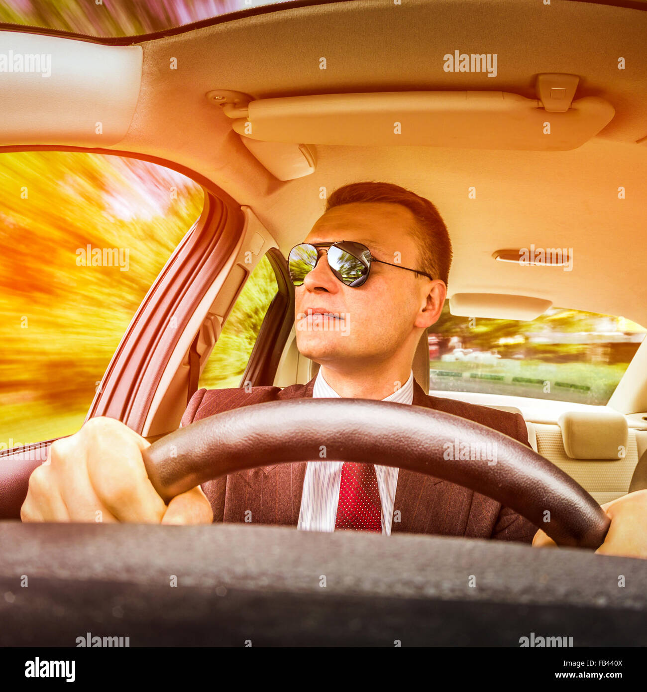 Mann in einem Anzug und Sonnenbrille auf einer Straße im Auto fahren. Stockfoto