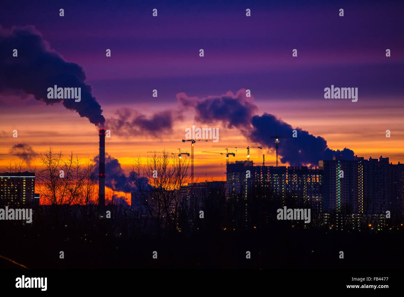 Moderne Stadt am Abend bei Sonnenuntergang. Rauch kommt aus den Rohren von Kraftwerken und Fabriken des modernen Viertels auf t Stockfoto