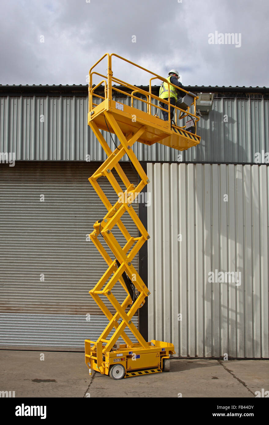 Ein Arbeiter verwendet eine kleine Industrie Scheren-Arbeitsbühne hohe Ebene Zugriff für elektrische Wartung Lager Stockfoto
