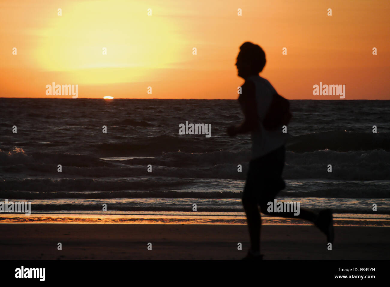 Umrisse eines Läufers bei Sonnenuntergang am Strand von Cable Beach, Broome, Western Australia mit hellen orange sky Hintergrund Stockfoto