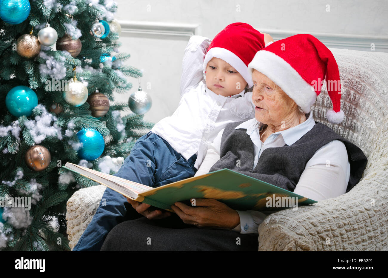 Ältere Frau ein Buch zu lesen, um ihren Enkel neben einem Weihnachtsbaum Stockfoto