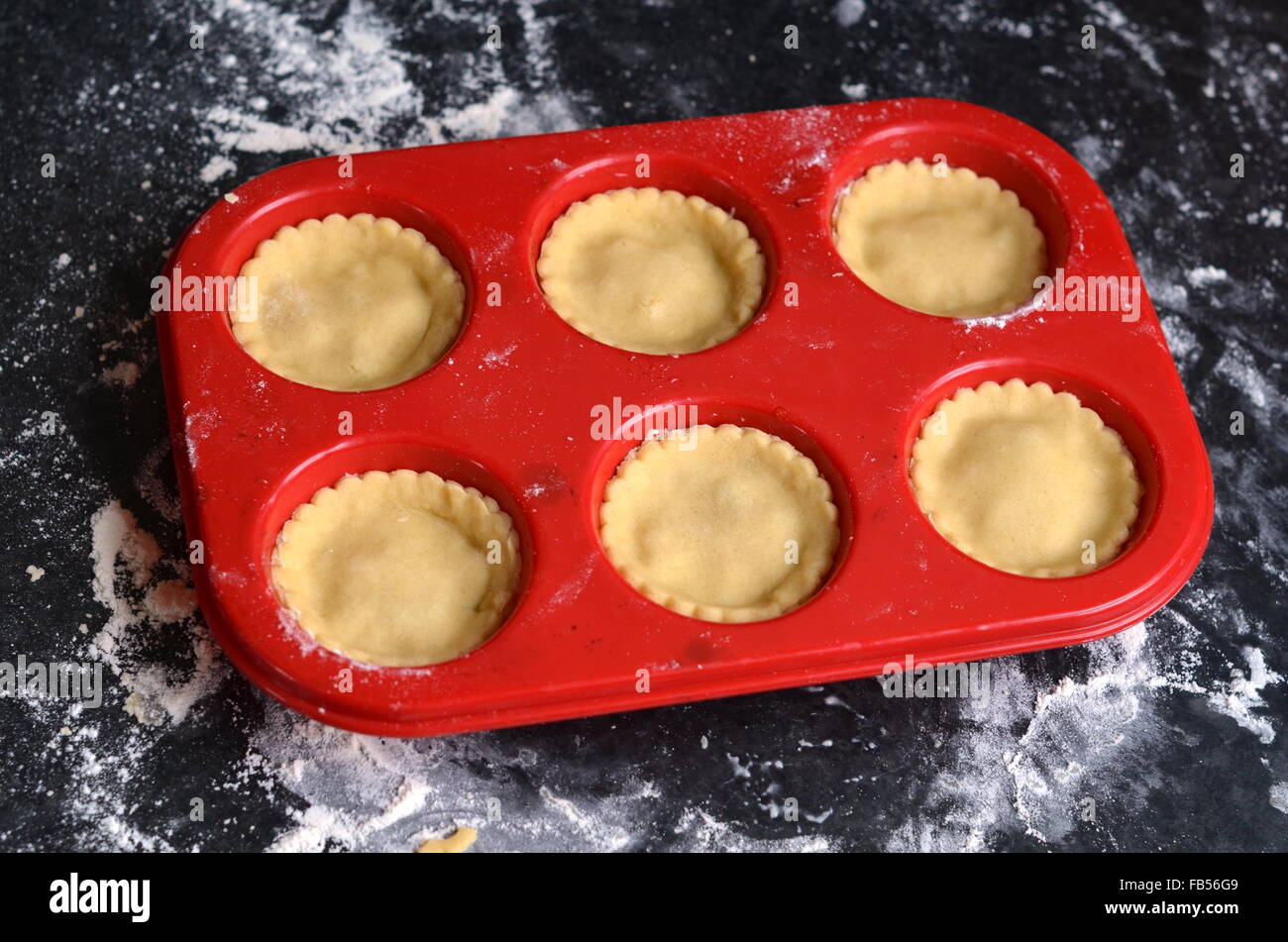 Rote Silikon Muffinbackblech mit ungebrannten Mince Pies auf einer dunklen bemehlten Arbeitsfläche Stockfoto