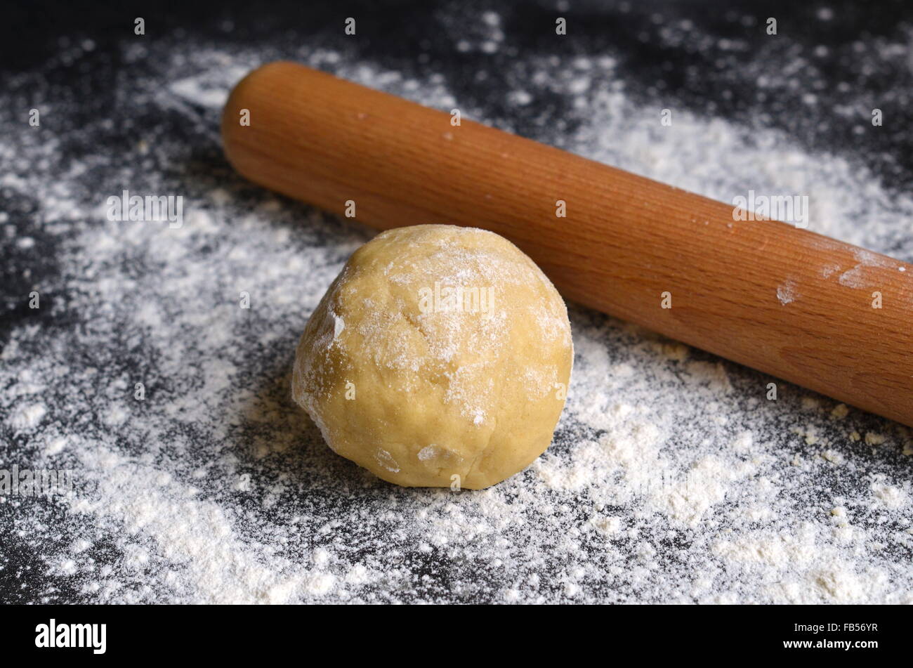 Eine Kugel aus Teig und einem hölzernen Nudelholz auf einem bemehlten dunkle Zähler nach oben Stockfoto