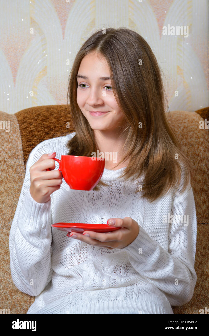 Ein Mädchen in einem weißen Pullover aus einer roten Tasse Tee zu trinken Stockfoto