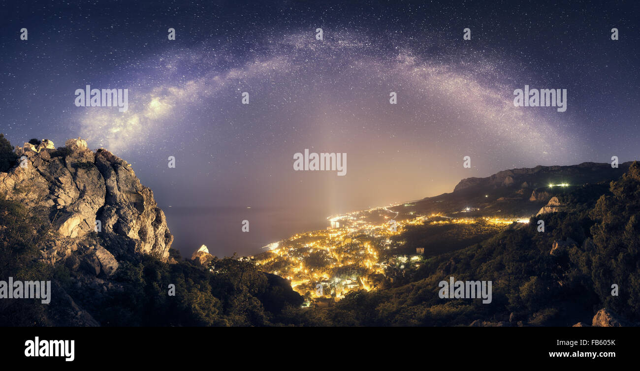 Schöne Nachtlandschaft mit Milky Way gegen die Lichter der Stadt, Berge, Meer und Sternenhimmel. Natur-Hintergrund Stockfoto