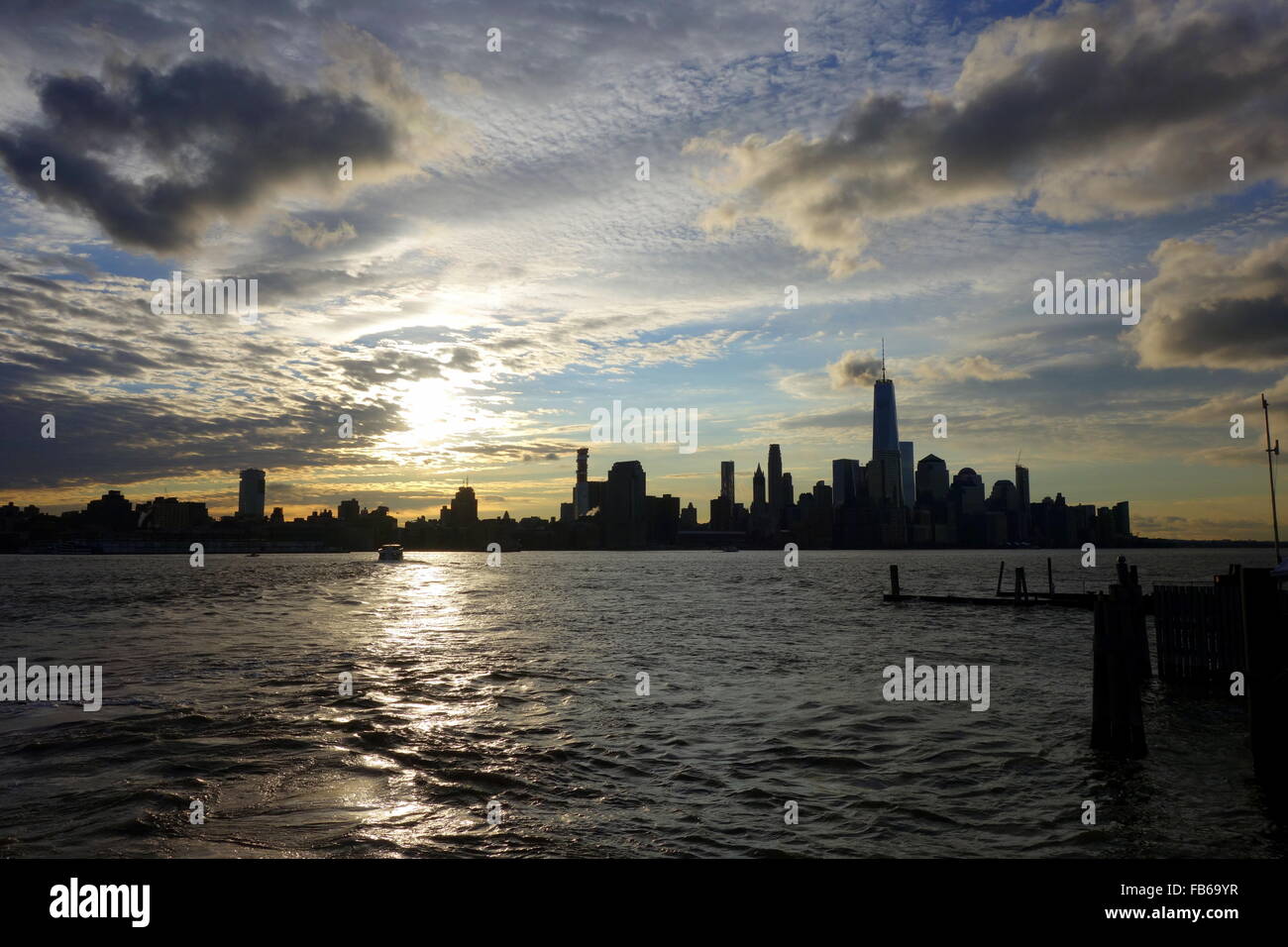 Bewegte Wolken und strahlende Sonne umrahmen Silhouetten der Skyline von New York City und des Freedom Tower, East River, New York, USA Stockfoto