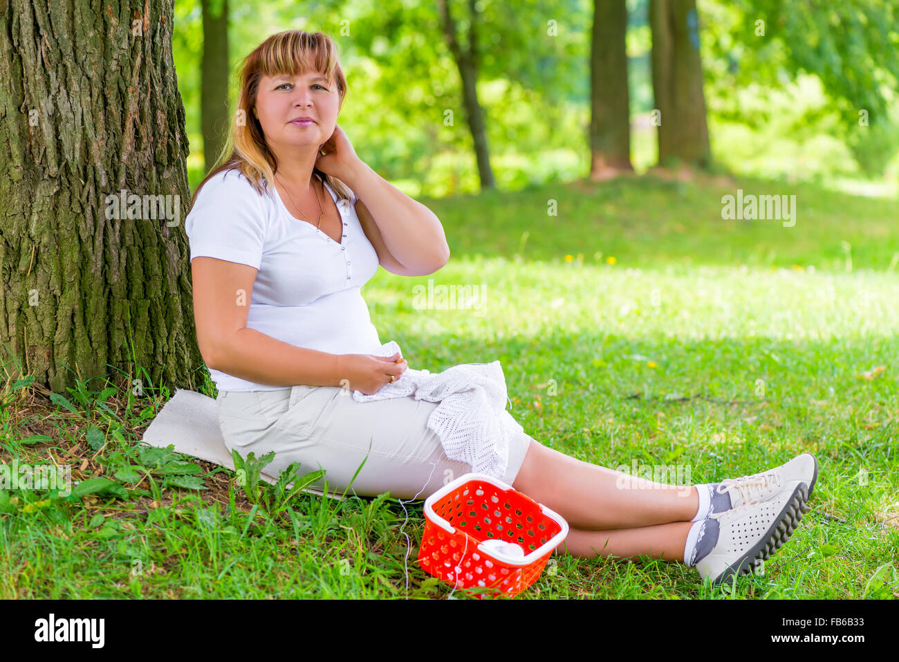 weiblich 50 Jahre tut, was er mag, sitzt neben dem Baum Stockfoto