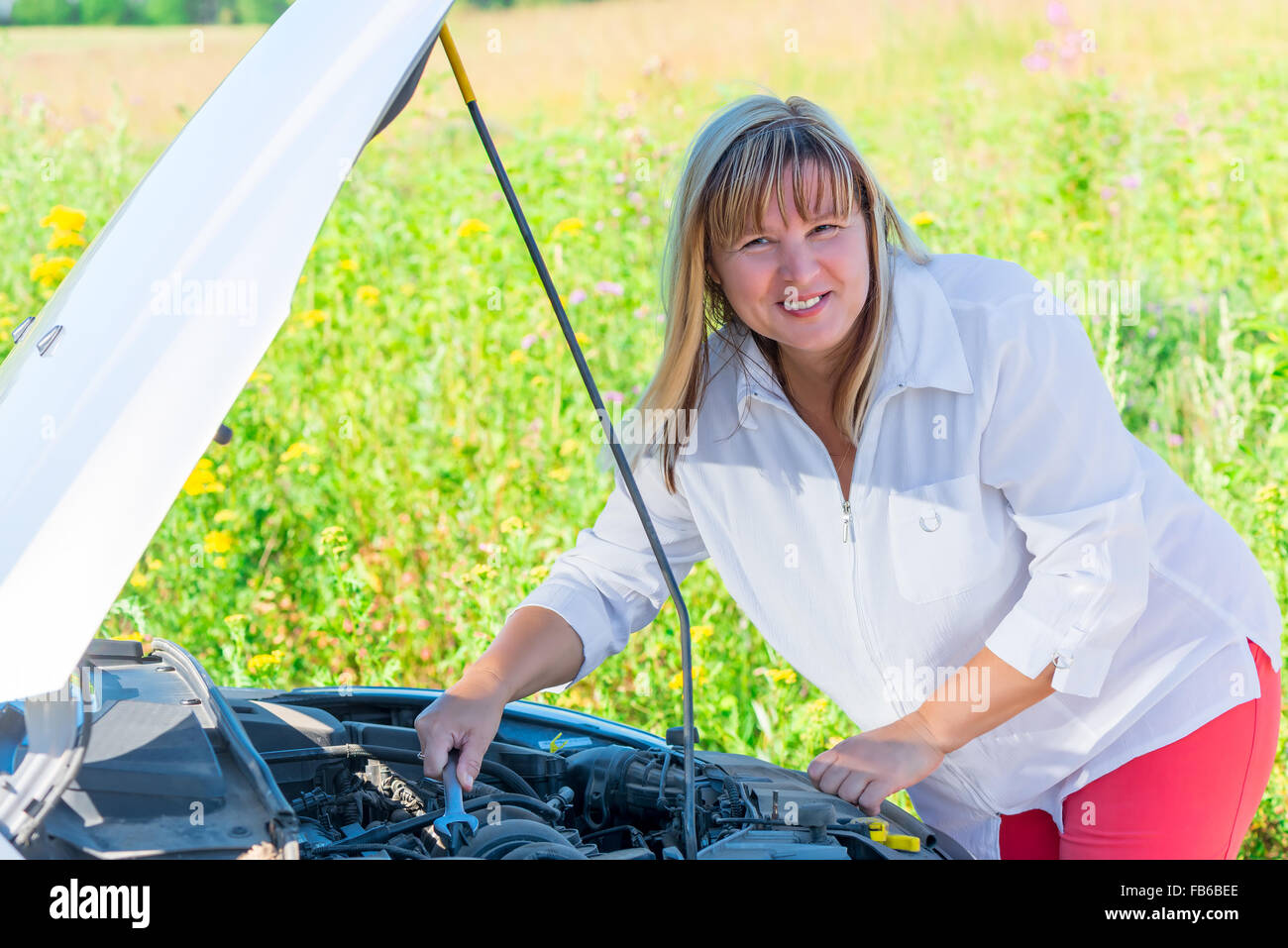 fröhliche Frau, die Reparatur des Autos auf einer leeren Straße Stockfoto