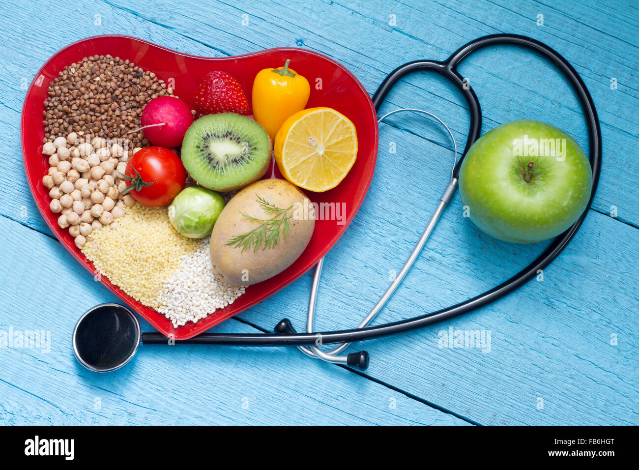 Lebensmittel auf Herz Teller mit Stethoskop Cardiology Konzept auf blauen Tafeln Stockfoto