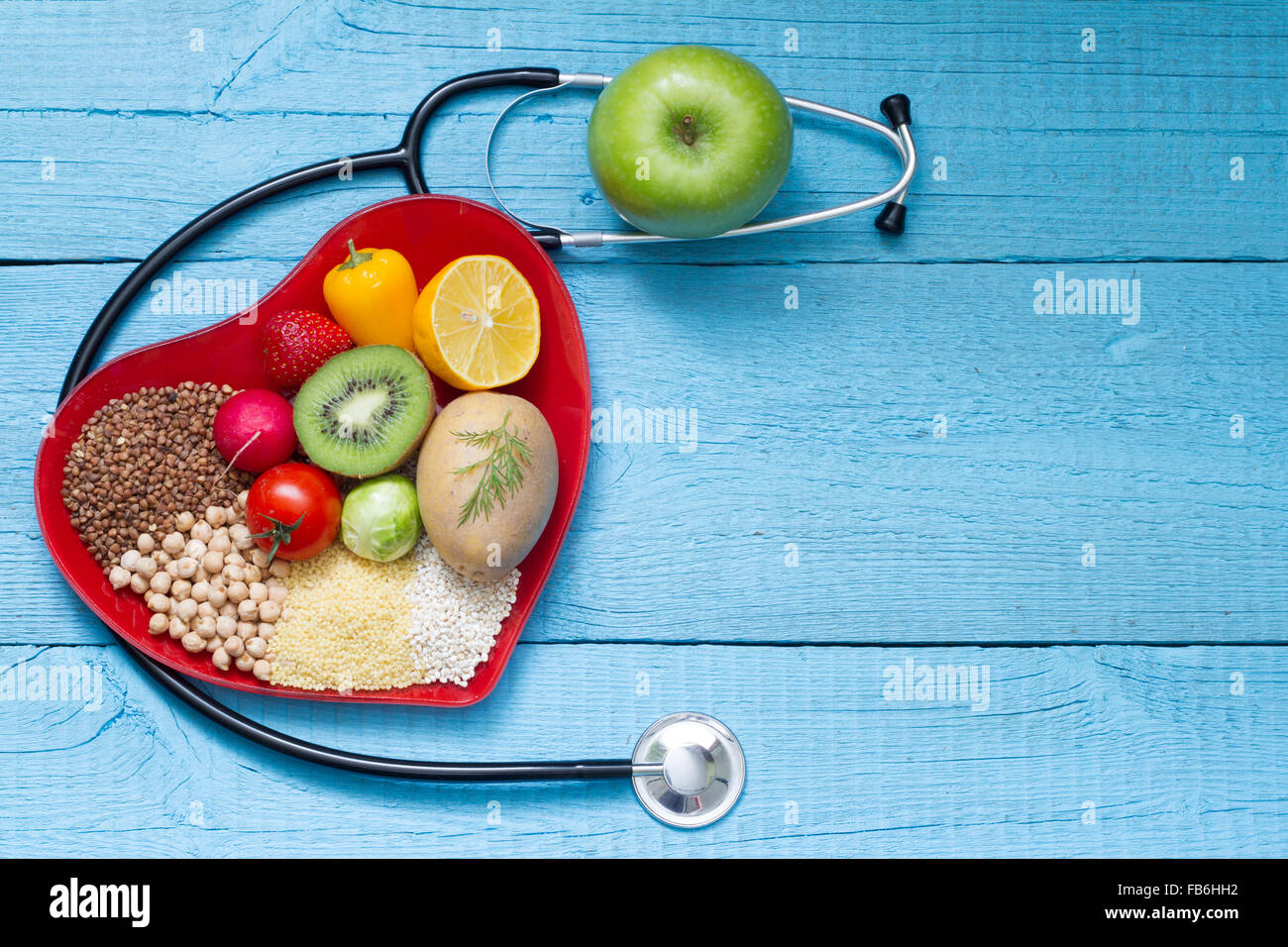 Lebensmittel auf Herz Teller mit Stethoskop Cardiology Konzept auf blauen Tafeln Stockfoto