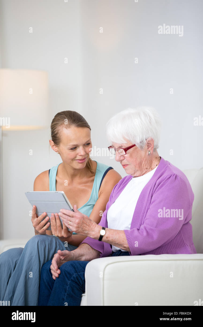 Oma mit ihrer Enkelin sitzen auf einem Sofa mit einem Tablet-Computer, lernen, wie man Technologie Stockfoto