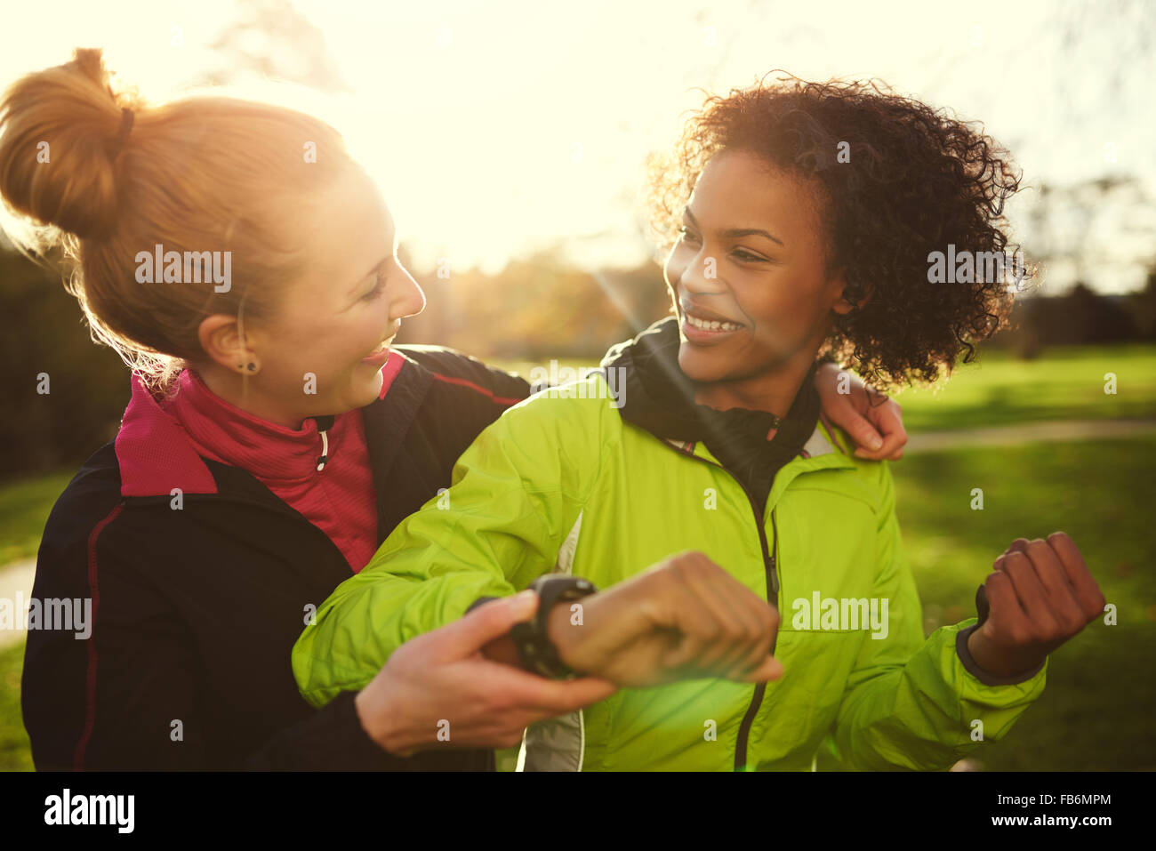 Zwei weibliche Athleten lächelnd und nach dem Training im sonnigen Park umarmt Stockfoto