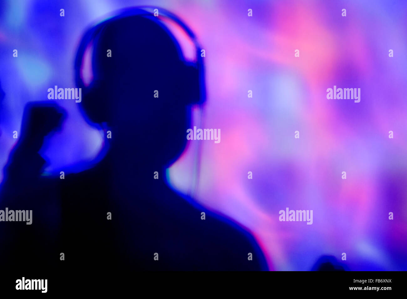 die Silhouette eines jungen Mannes mit Kopfhörern in einem Tanzclub mit bunten Lichtern Stockfoto