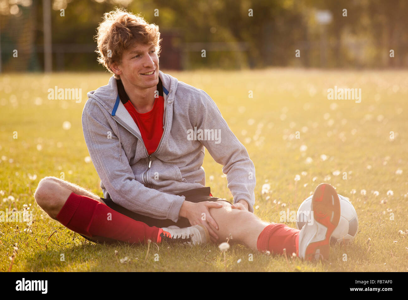 Lächelnde junge Fußball Spieler massierende Bein sitzend auf Feld Stockfoto