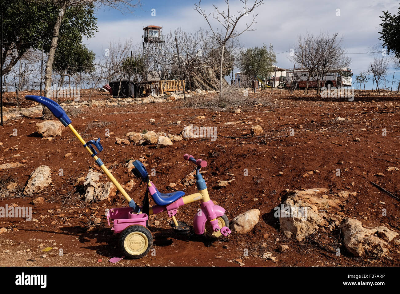 ESH Kodesh, West Bank. 11. Januar 2016. Ein Dreirad auf der Seite der Straße im Esh Kodesh israelischen Außenposten im Westjordanland in der Nähe von Shilo, unter der Jurisdiktion des Regionalrats Mateh Binyamin. Der Wachturm von IDF Soldaten bemannt ist im Hintergrund sichtbar. Die Siedlung wurde 1999 gegründet und beherbergt heute rund 40 Familien, die es einer nicht autorisierten Gemeinschaft von Shilo betrachten, in den Prozess der immer offiziell autorisiert. Stockfoto