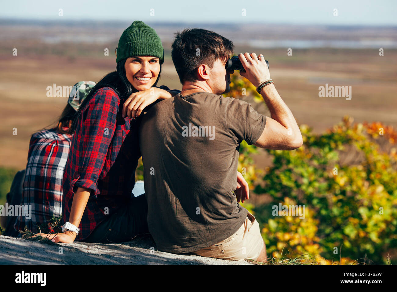 Glückliche junge Frau sitzt mit Freund mit dem Fernglas im Wald Stockfoto