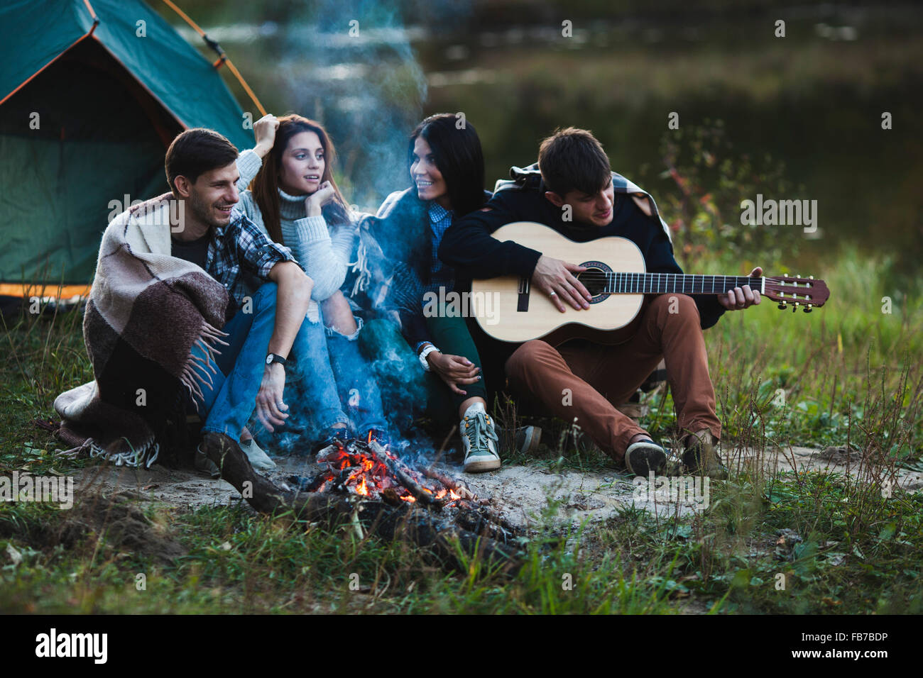 Mann, die Gitarre zu spielen, während Sie mit Freunden am Lagerfeuer sitzen Stockfoto